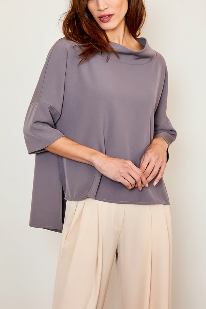 Woman wearing a gray blouse and beige pants against a beige wall.