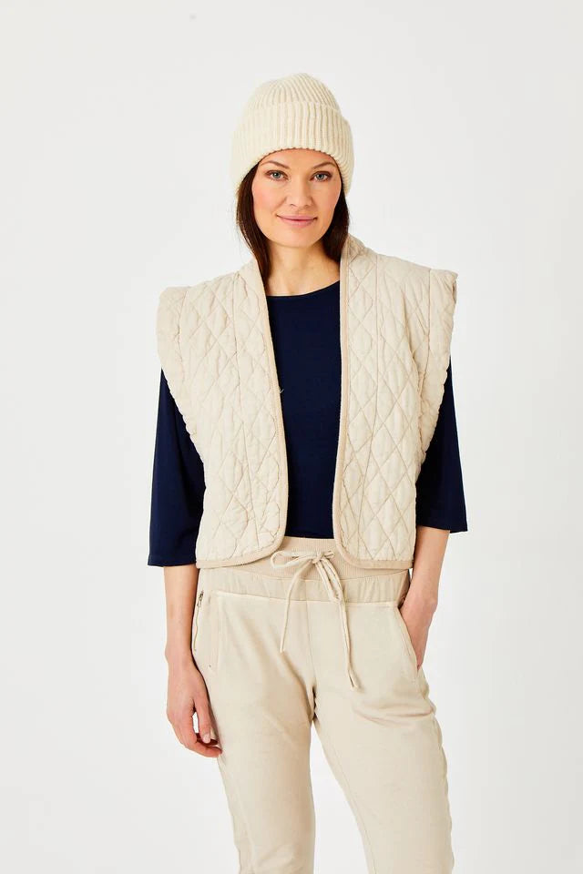 Woman wearing a cream quilted vest, beanie, and pants on a white background